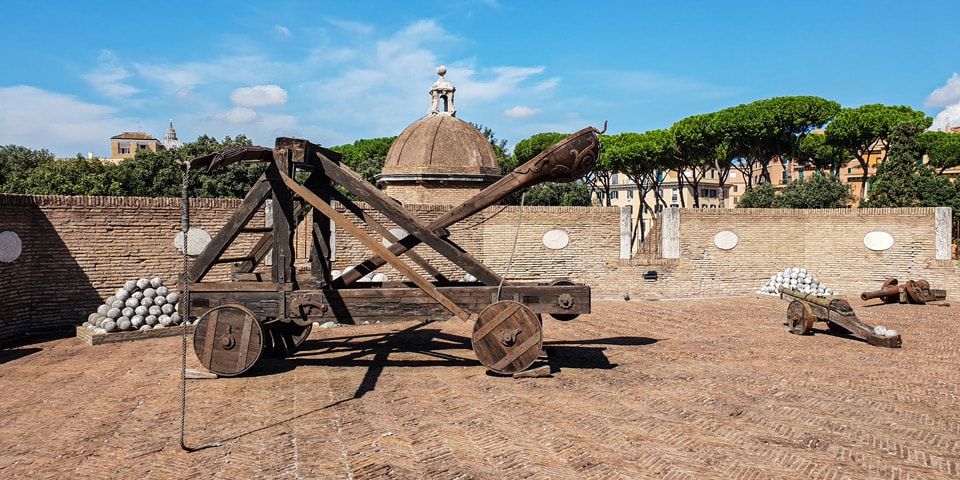 Catapulte reconstituée et boulets de pierre empilés sur les remparts du Château Saint-Ange, avec le dôme de la Basilique Saint-Pierre à l’arrière-plan, à Rome