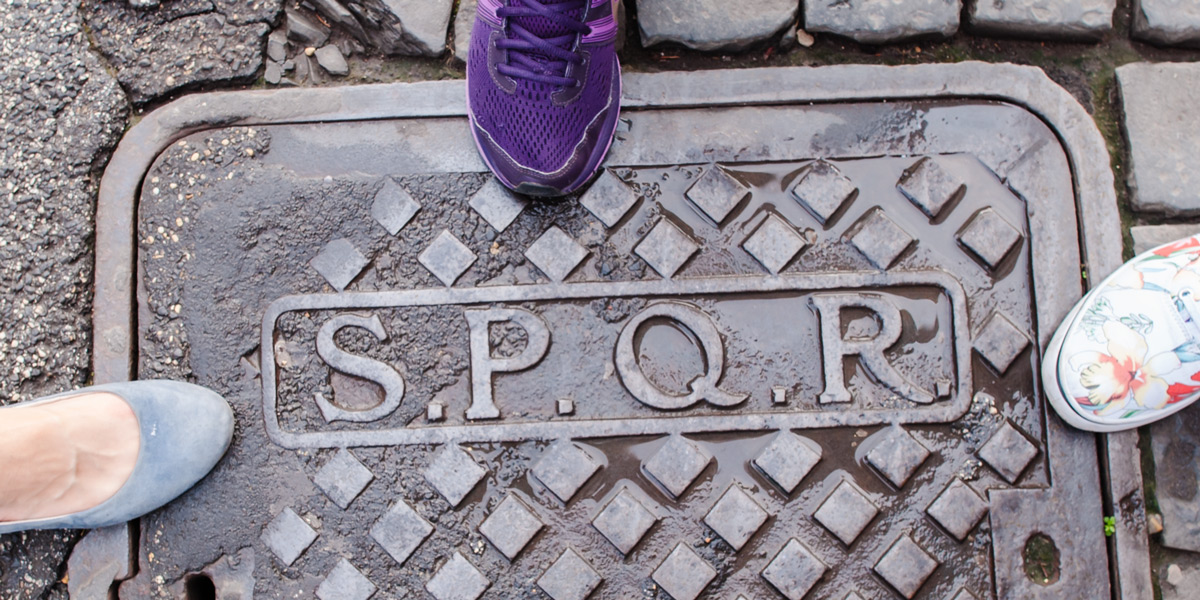 Initiales SPQR sur une plaque d’égout métallique dans une rue pavée de Rome